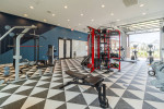Modern fitness center with gym equipment and large windows in a gated apartment community.