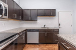 Modern kitchen with dark cabinets, granite countertops, and stainless steel appliances in C Street Flats apartment.