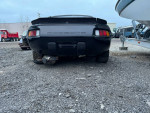 Rear view of a 1985 Porsche 928 S on a gravel surface, showcasing its sporty design.