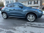 2013 Nissan Juke SV in blue, featuring alloy wheels, parked on the street with a house in the background.