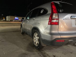 Side view of a silver 2008 Honda CRV for sale, showcasing its rear and wheels under night lighting.