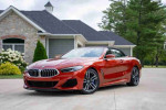 2020 BMW M850i xDrive convertible in Sunset Orange Metallic parked in front of a house.