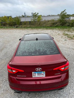 Rear view of a 2015 Hyundai Sonata Limited in red with a sleek design, parked on gravel.