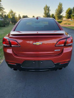 Rear view of a 2015 Chevrolet SS in red color parked outdoors with trees in the background.