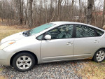 Silver 2005 Toyota Prius hatchback parked on gravel, showing minor rust and damaged exhaust.