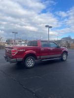 2013 Ford F-150 Lariat 4WD truck in red with spacious crew cab and hard tonneau cover, parked outdoors.