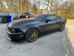 2013 Ford Mustang GT Premium in matte black finish parked on driveway with stock hood and wheels