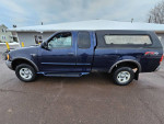 2002 Ford F-150 pickup truck in blue with a truck cap parked on a snowy road.