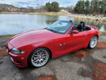 Beautiful red BMW Z4 M Roadster parked by a serene lake, showcasing its low mileage and stylish design.