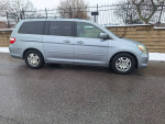 Silver Honda Odyssey EXL minivan with low mileage parked on a wet road, showcasing its clean condition and features.