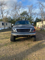 2002 Ford F150 with a small lift, in need of repair, parked on grass.