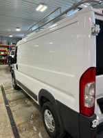 Left side view of a 2017 Ram Promaster 1500 with ladder rack and bright white exterior in a garage