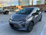 2023 Chevrolet Bolt 2LT in Gray Ghost Metallic parked outdoors with shops in the background