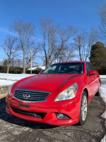 2010 Infiniti G37x AWD in red, parked on a snow-covered driveway with trees in the background.