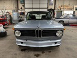 Front view of a 1972 BMW 2002 Tii project car in a workshop, showcasing its classic design and condition.