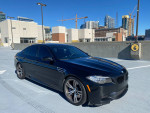 2014 BMW M5 sedan in excellent condition, parked on rooftop with city skyline in background.