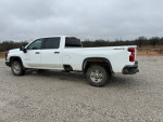 2021 Chevrolet Silverado 2500HD work truck in white, showcasing its crew cab and long bed design on gravel terrain.