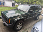 2001 Jeep Cherokee Sport in green, parked on a driveway, showcasing its robust exterior and off-road tires.