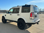 White 2013 Land Rover LR4 HSE Luxury parked with a clear blue sky, showcasing its sleek design and off-road tires.