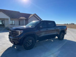 2022 GMC Sierra 1500 AT4X 4WD in black color with off-road tires parked in front of a house.