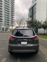 Rear view of a 2013 Ford Escape SEL in Sterling Gray Metallic parked in a modern outdoor setting.