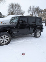 2014 Jeep Wrangler Sahara 4WD in snowy setting, showcasing its exterior and tires with minimal wear.