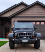 Front view of a 2011 Jeep Wrangler Sport 4WD parked in driveway, showcasing new headlights and rugged design.