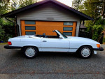 1986 560SL Mercedes classic convertible parked outside a modern home, showcasing its sleek design.