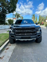 Front view of a black 2020 Ford F-150 Raptor 4WD parked on a street with palm trees.