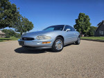 1997 Buick Riviera Supercharged coupe parked on a sunny street, featuring chrome wheels and a sleek silver finish.