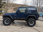2000 Jeep Wrangler Sport 4WD in blue, showcasing tires and off-road features, parked outdoors.