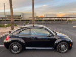 Side view of a black 2016 Volkswagen Beetle Coupe parked, showcasing its compact design and sleek profile.