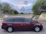 2016 Honda Odyssey SE mini-van in burgundy color parked in a park setting, showcasing its sleek design.