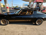 1980 Chevrolet Camaro Z28 in black with gold accents parked at a gas station, showcasing its classic design.