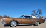 Side view of a 1970 Lincoln Continental Mark III in brown with a white convertible top against a clear blue sky.