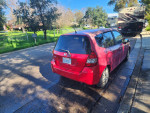 2007 Honda Fit in red parked on the street, featuring a manual transmission and spacious cargo area.