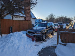2002 Jeep Grand Cherokee with snow plow parked in snowy driveway, ready for winter tasks